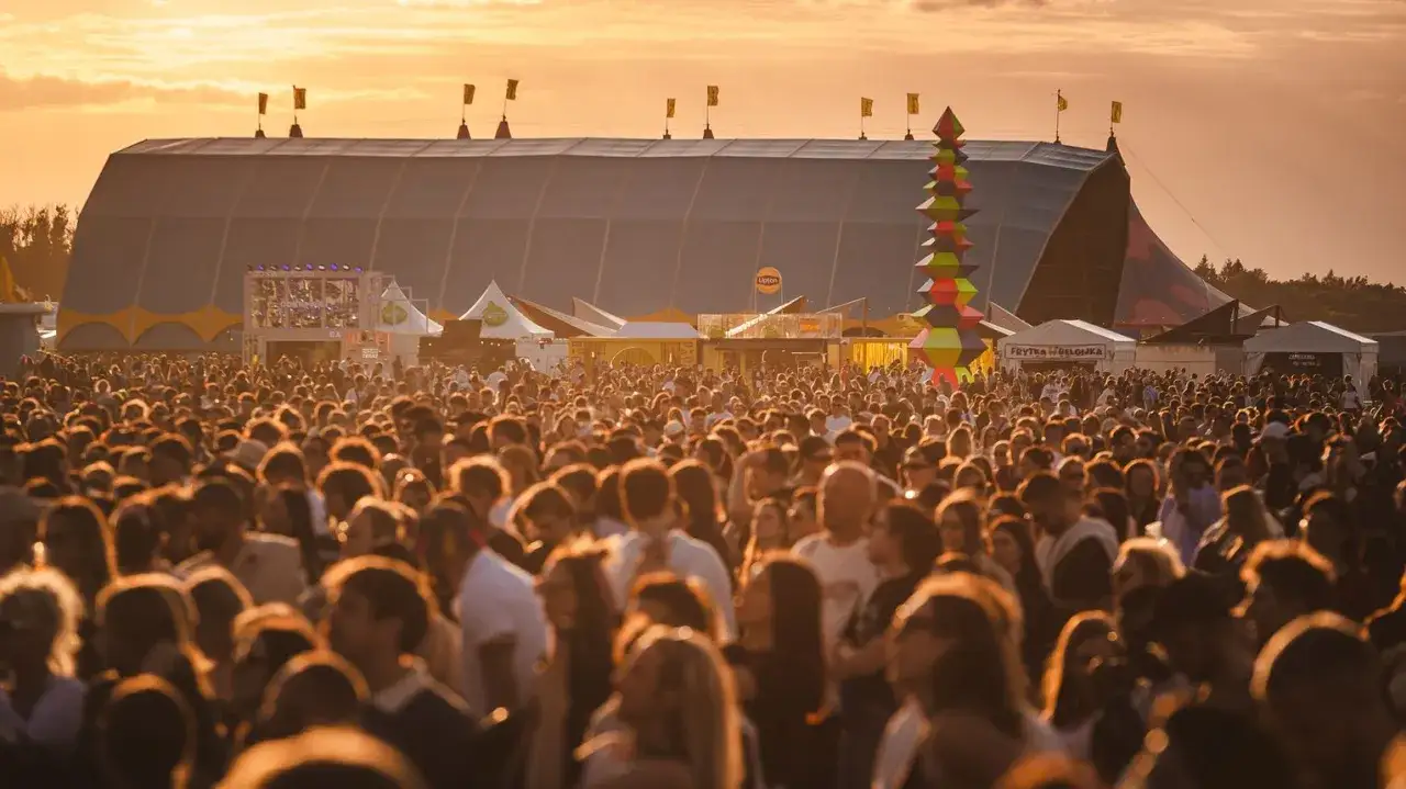 Tłum ludzi na festiwalu, zachód słońca, wielki namiot i kolorowa instalacja. Kto będzie następny na scenie?