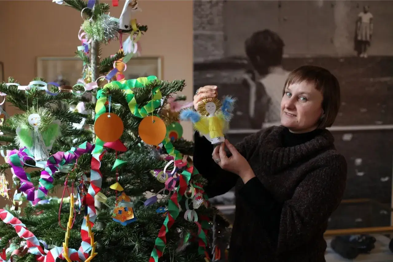 Kiedy zdjąć ozdoby świąteczne? Kobieta trzyma aniołka, a choinka jest udekorowana kolorowymi łańcuchami i bombkami.