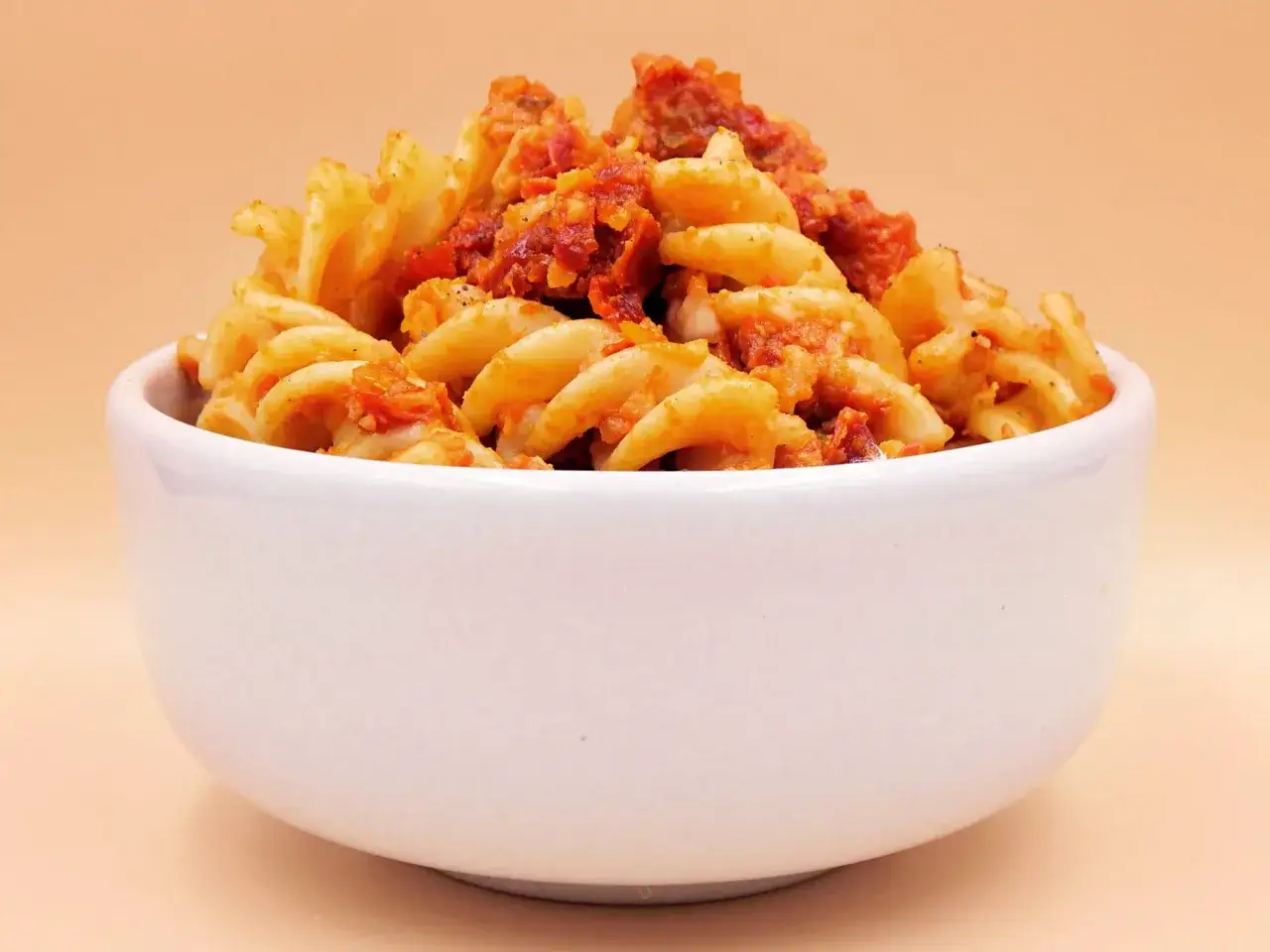 Fusilli makaron z aromatycznym pesto i kawałkami pomidorów, podany w białej miseczce.