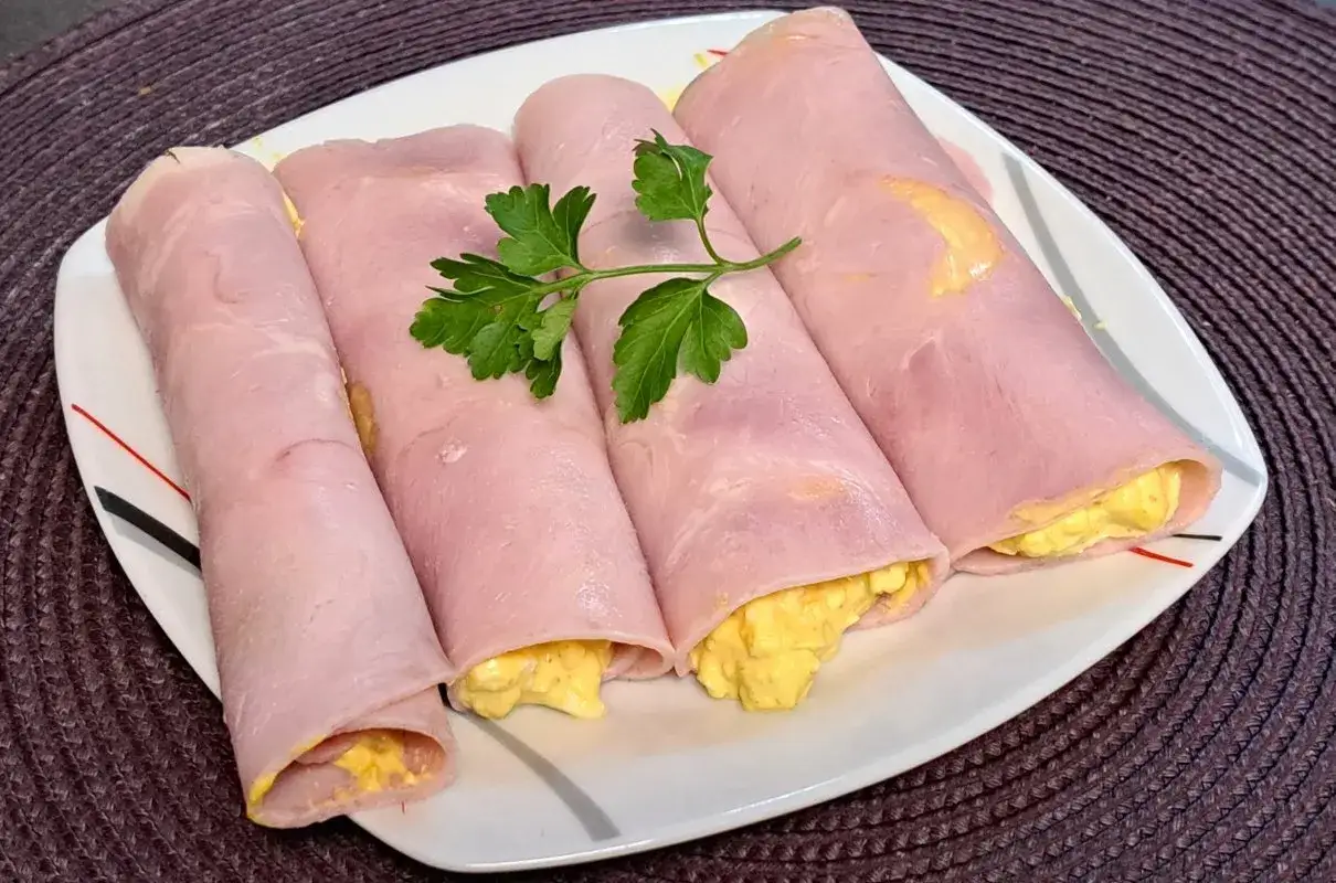 Roladki z szynki z pastą jajeczną, ozdobione natką pietruszki. Pyszna przekąska, idealna na każdą okazję.