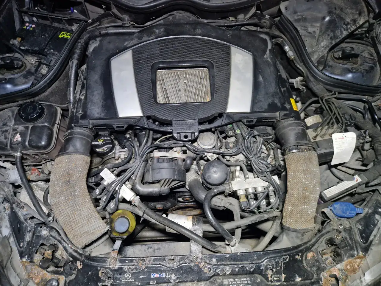 Silnik Mercedesa CLK W209, widok z góry. Widać elementy układu dolotowego, akumulator, przewody i inne podzespoły.