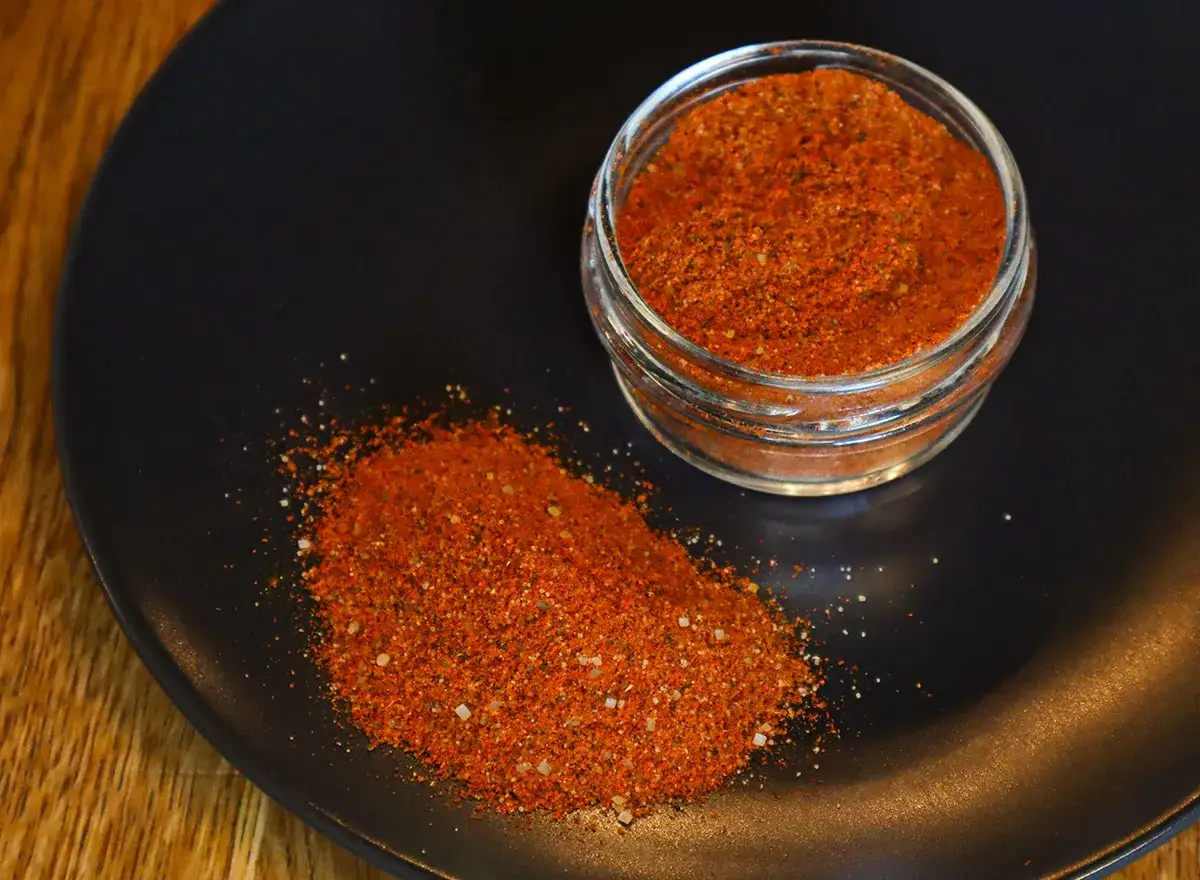 Sypka przyprawa do burgerów w słoiczku i rozsypana na talerzu. Idealna do grillowania i nadania smaku mięsu.