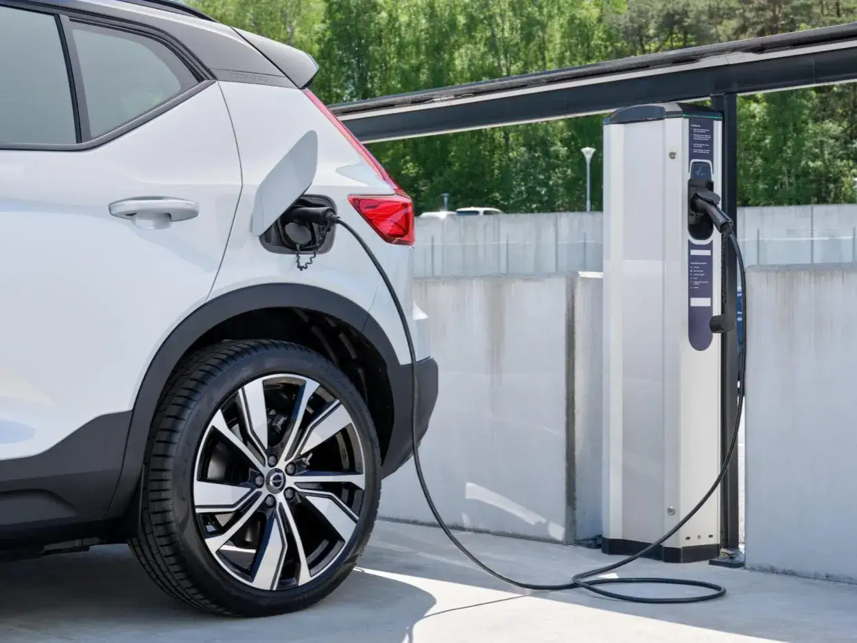 Biały samoch&oacute;d plug-in hybrid, czyli taki, kt&oacute;ry można ładować z gniazdka, jest podłączony do ładowarki.