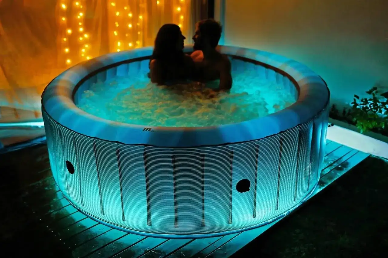 Para relaksu w jacuzzi. Para przytula się w bąbelkującej wodzie, otoczona niebieskim światłem i ciepłymi lampkami.