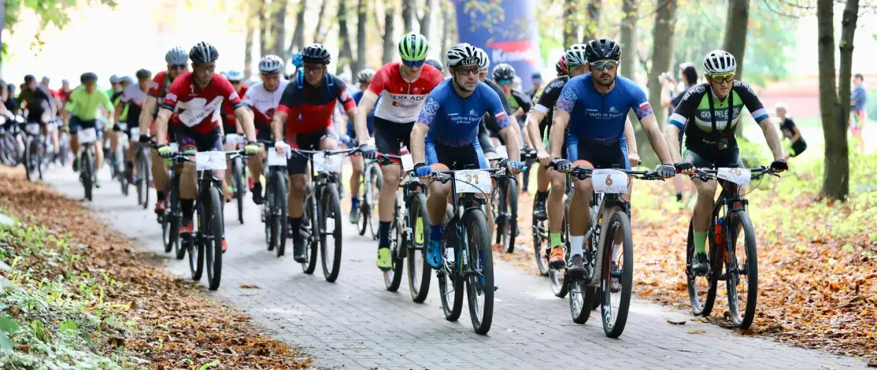 Grupa kolarzy ściga się w maratonie rowerowym wśród jesiennych liści.