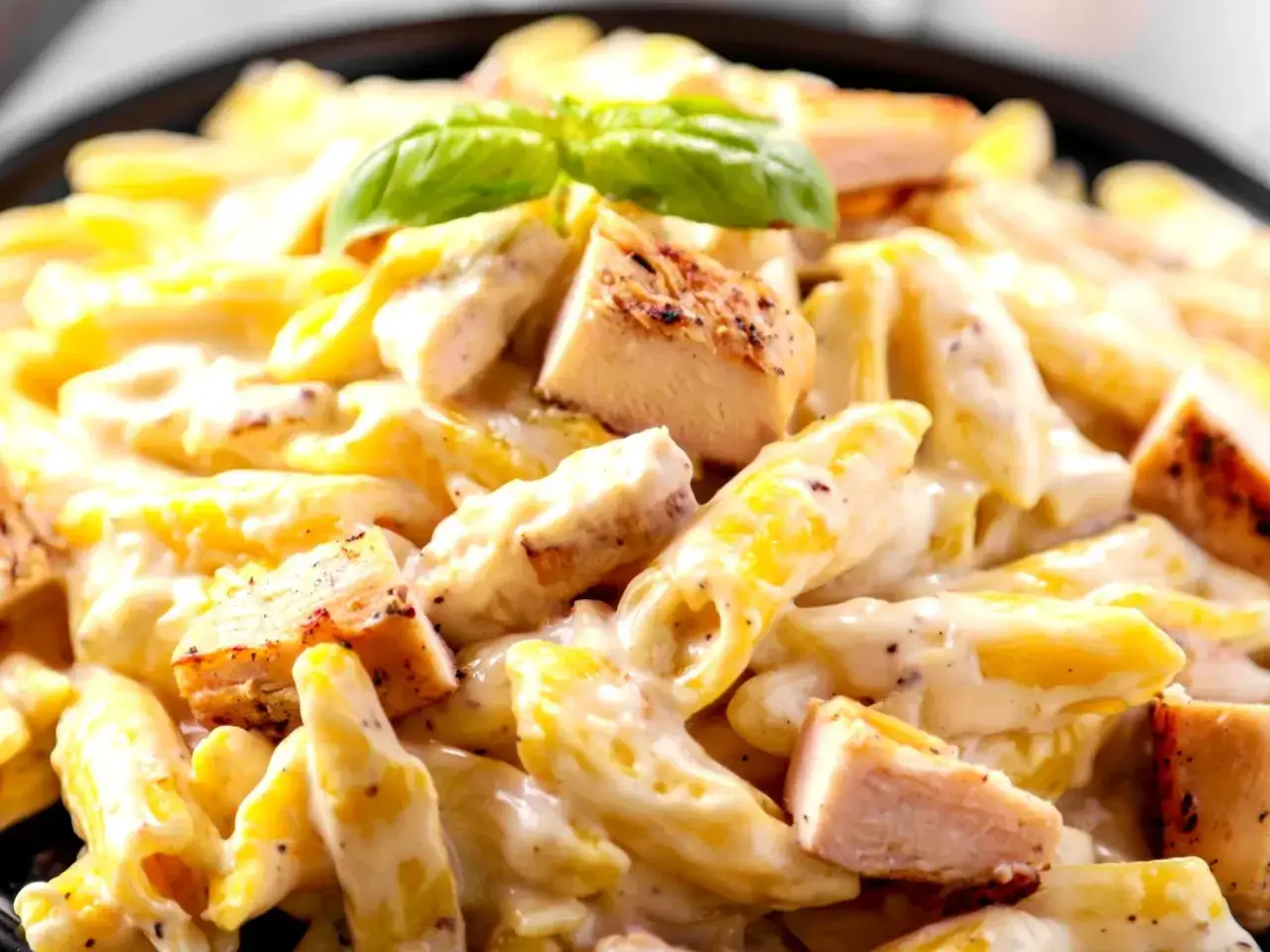 Penne z kurczakiem w kremowym sosie, idealne na piątkowy obiad zamiast ryby. Udekorowane listkiem bazylii.