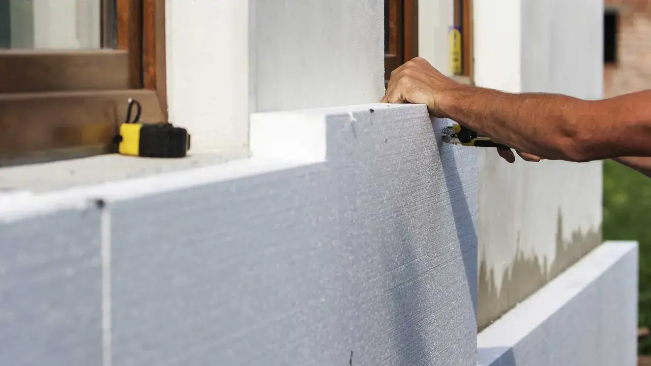 Ręczne cięcie styropianu do naprawy elewacji. Narzędzia i materiały budowlane w użyciu.