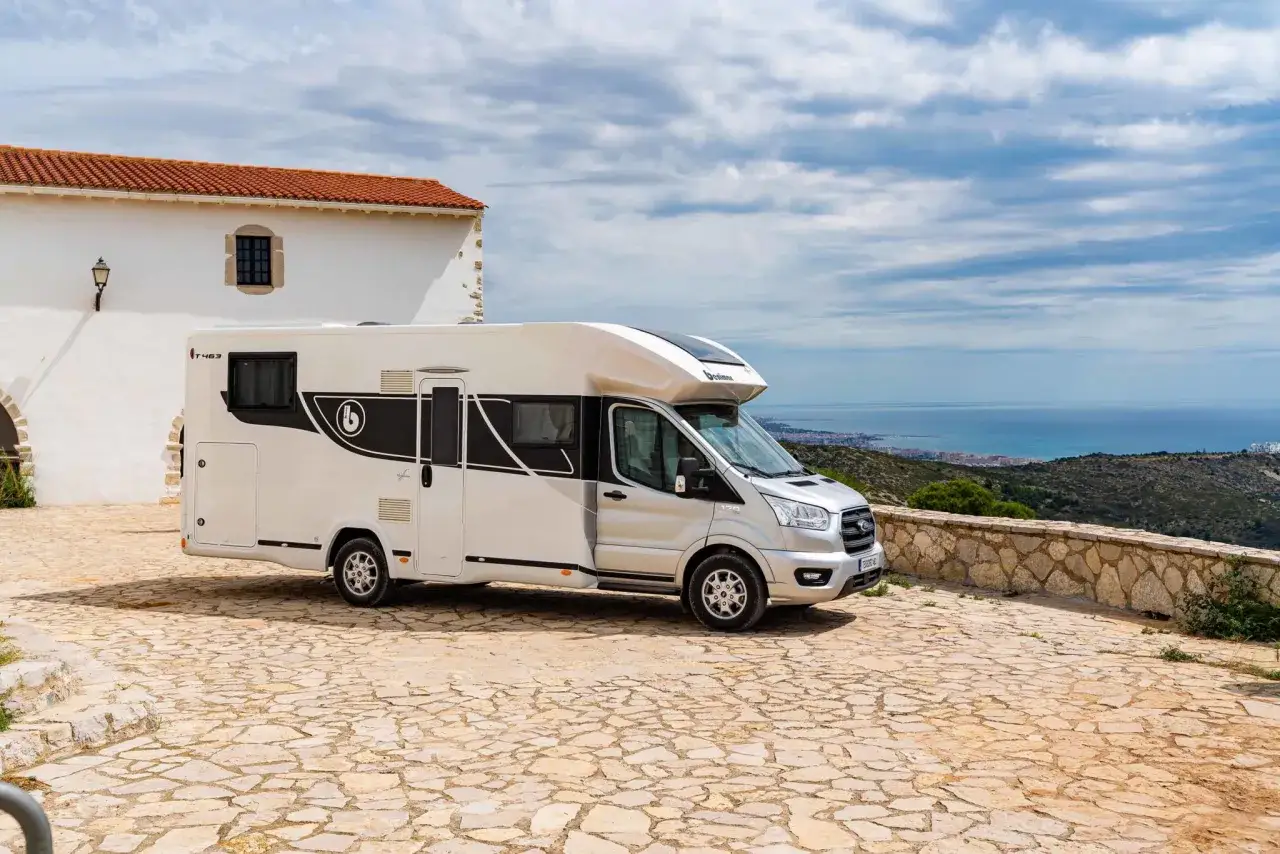 Kamper 4 osobowy zaparkowany na kamiennym placu z widokiem na morze i miasto. Idealny na wakacyjne podróże.