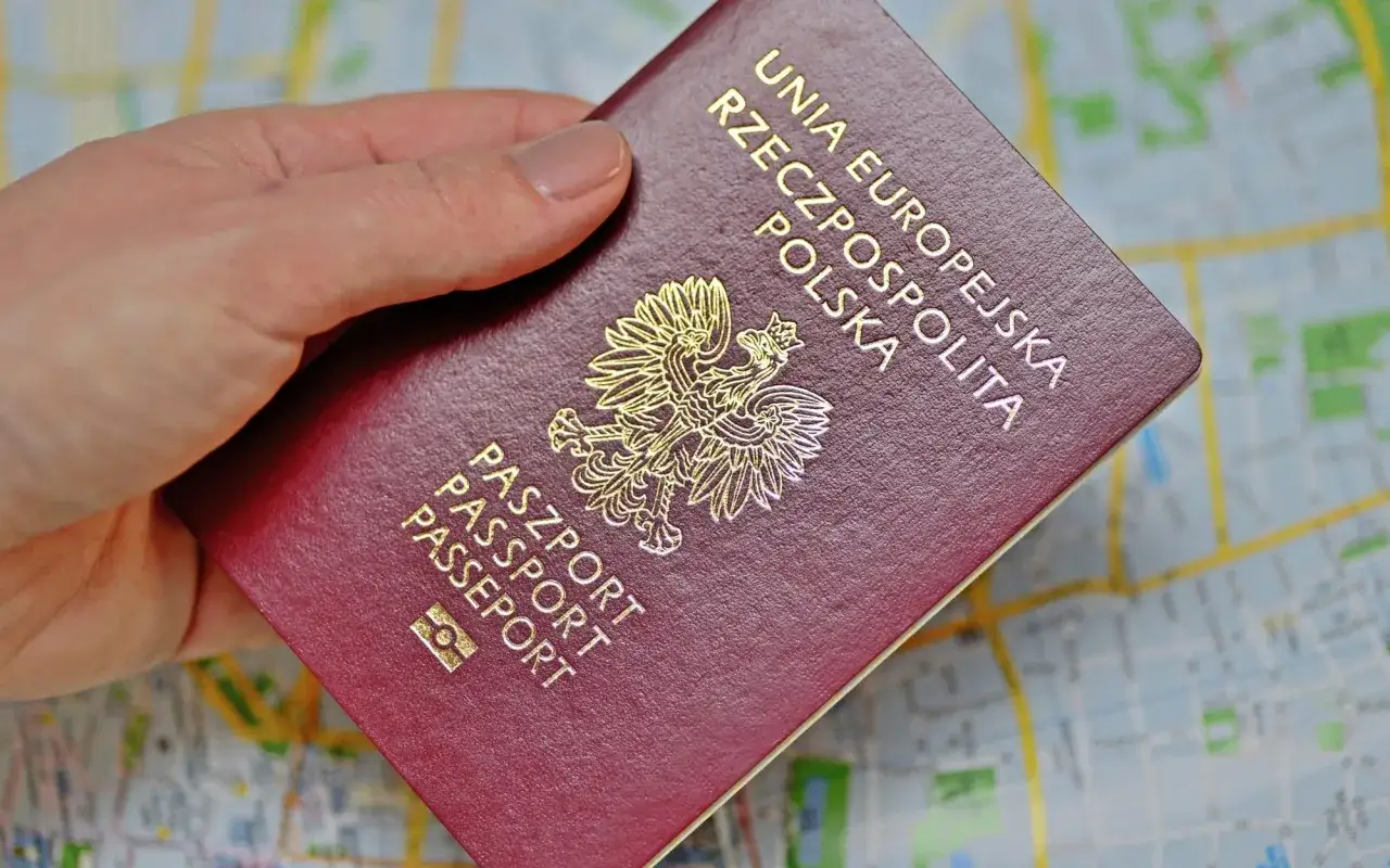 Dłoń trzyma polski paszport na tle mapy. Brak dowodu osobistego za granicą konsekwencje mogą być poważne.