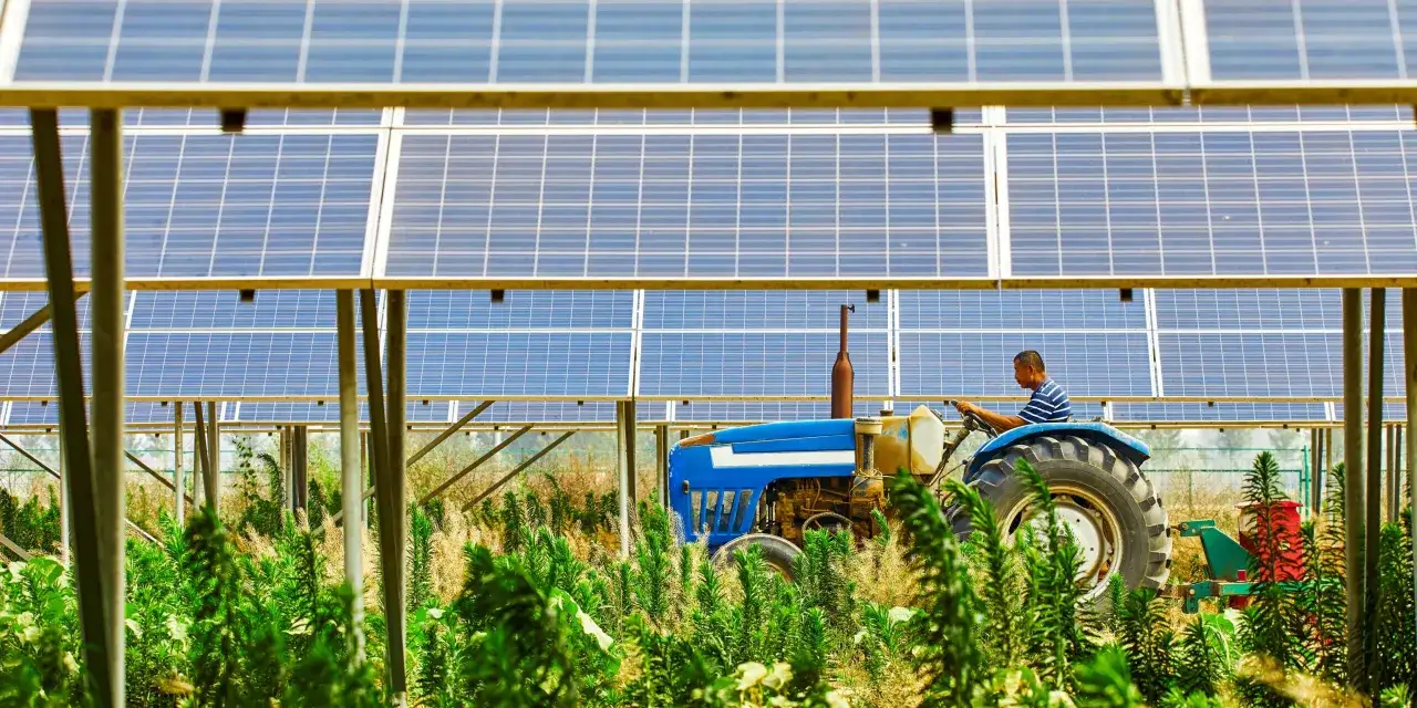 Rolnik na niebieskim traktorze pod panelami fotowoltaicznymi. Nowoczesne rolnictwo zasilane słońcem.