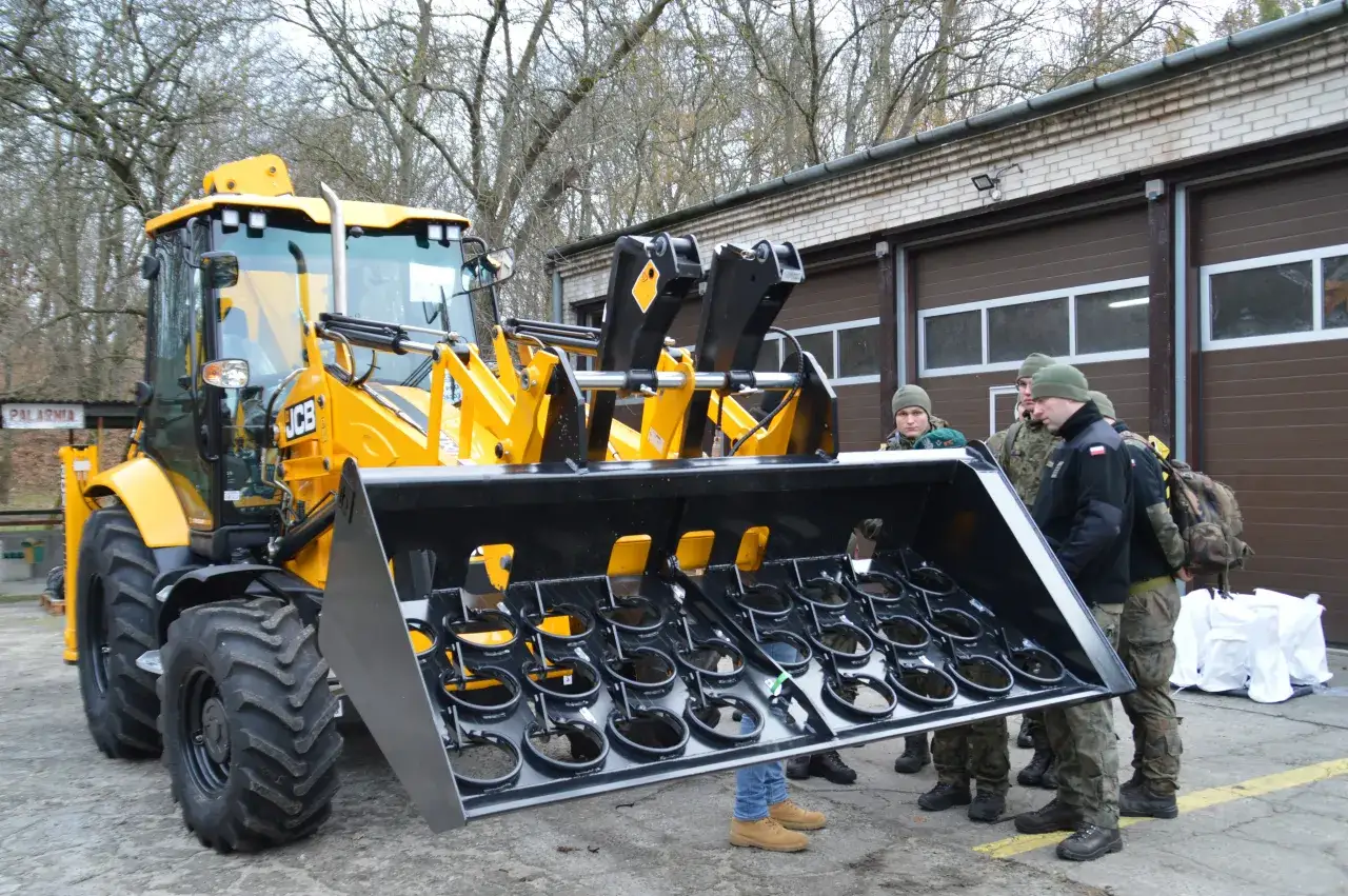 Żółta koparko-ładowarka JCB z szeroką łyżką, obok żołnierze. Zastanawiasz się, jaką koparko ładowarkę kupić?