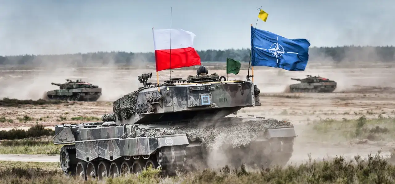 Czołg z polską i NATO-wską flagą, symbolizujący partnerstwo dla pokoju, w akcji na poligonie.