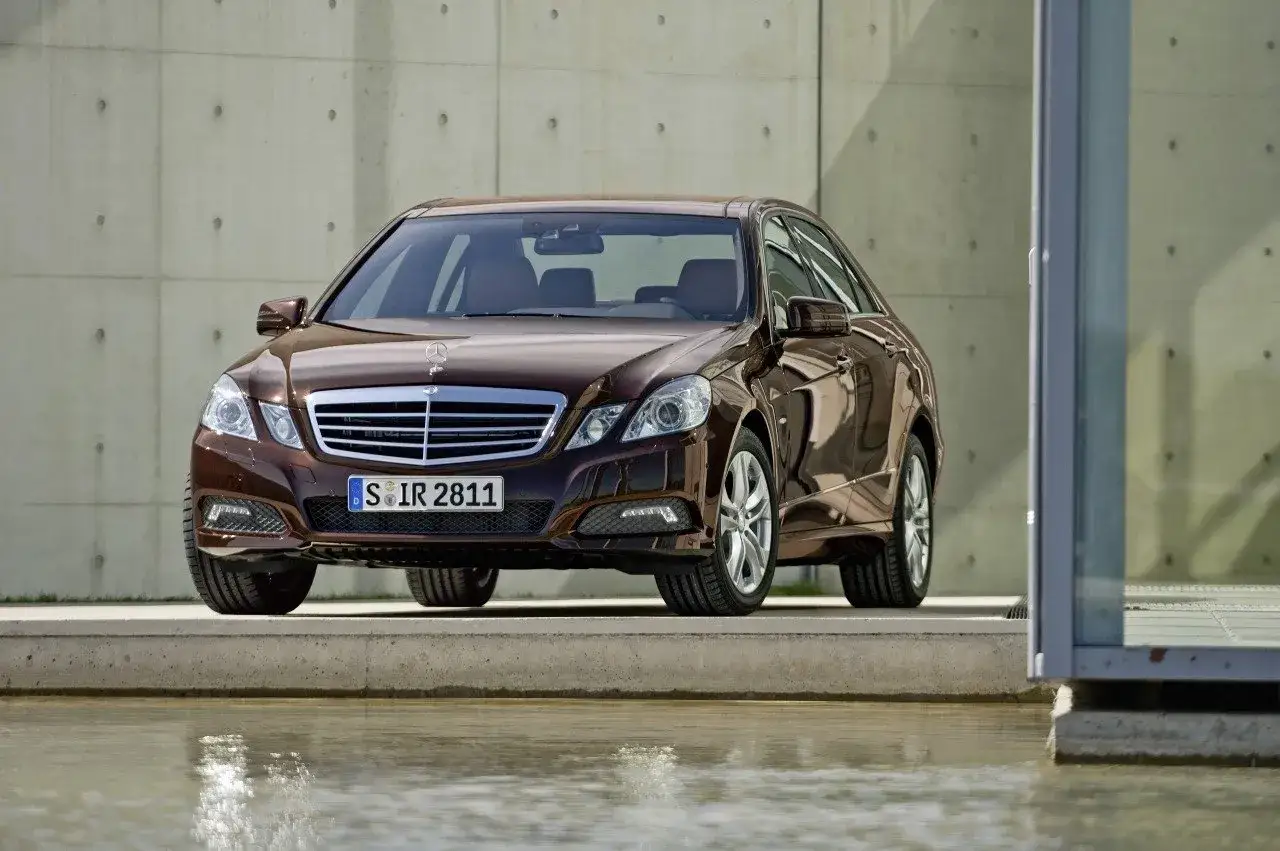 Elegancki brązowy Mercedes-Benz Klasa E z chromowanym grillem stoi przed betonową ścianą.