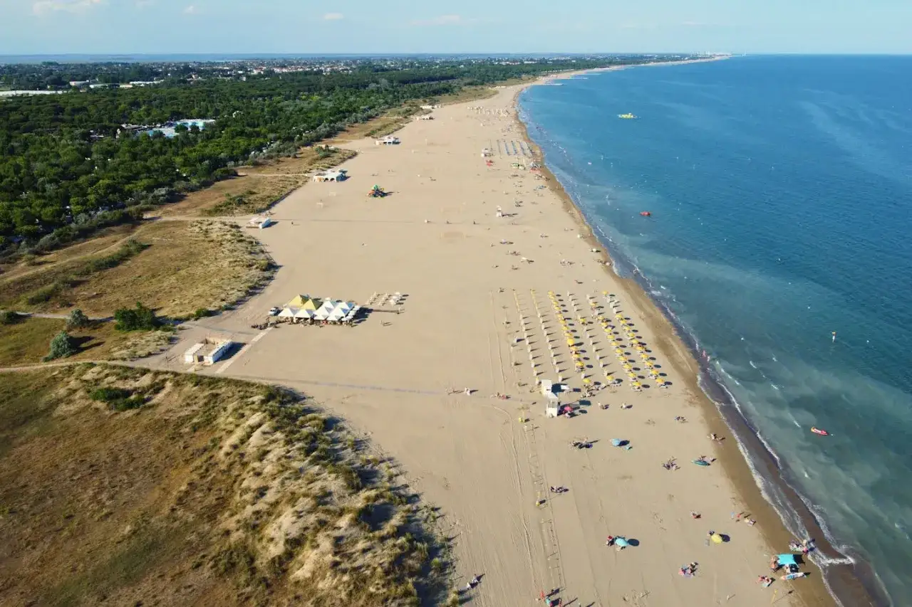 Słoneczna plaża w Marina di Venezia Camping, z rzędami parasoli, zielenią i turkusowym morzem.