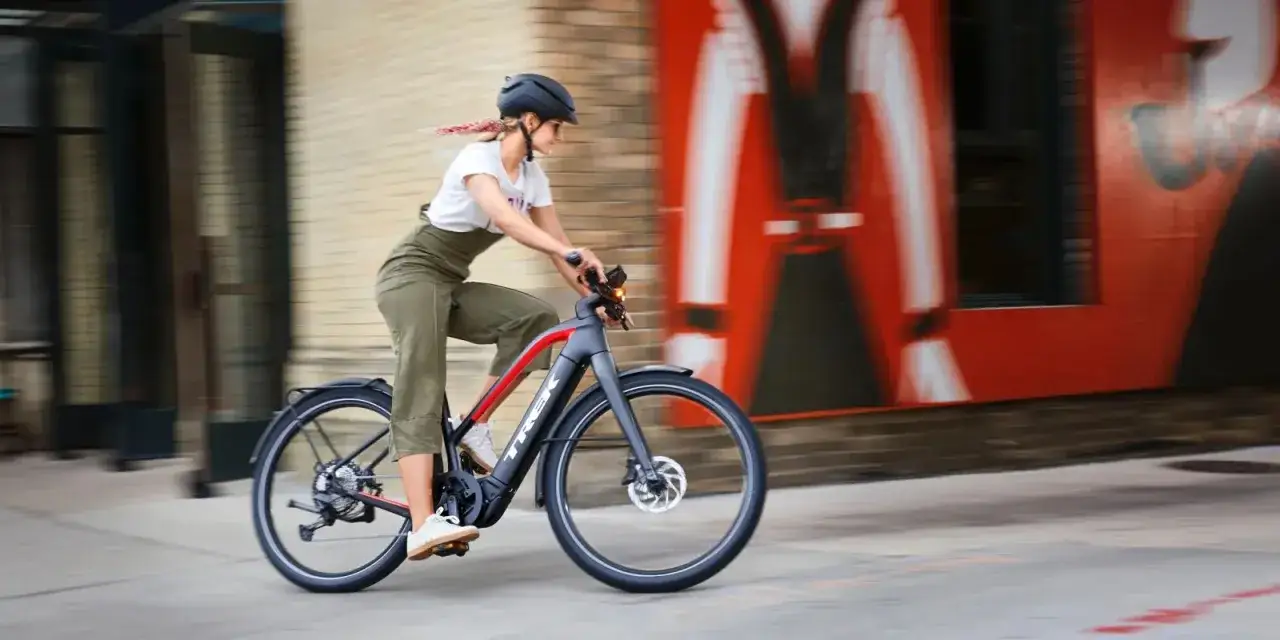 Kobieta w kasku jedzie rowerem elektrycznym, który wspomaga jazdę. Widać silnik i baterię, które pokazują, jak działa rower elektryczny.