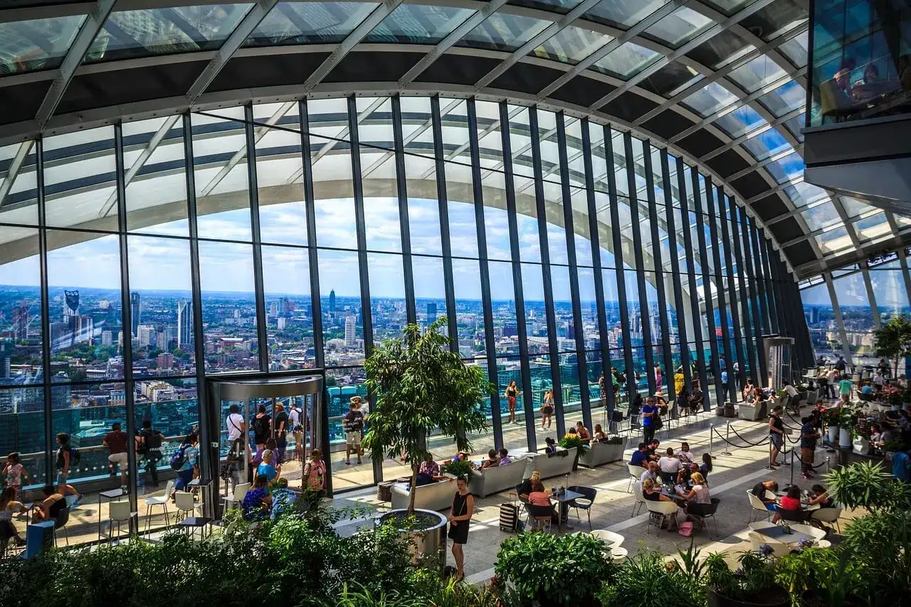 Wnętrze Sky Garden w Londynie z widokiem na miasto. Ludzie relaksują się wśr&oacute;d zieleni, pod szklanym dachem.
