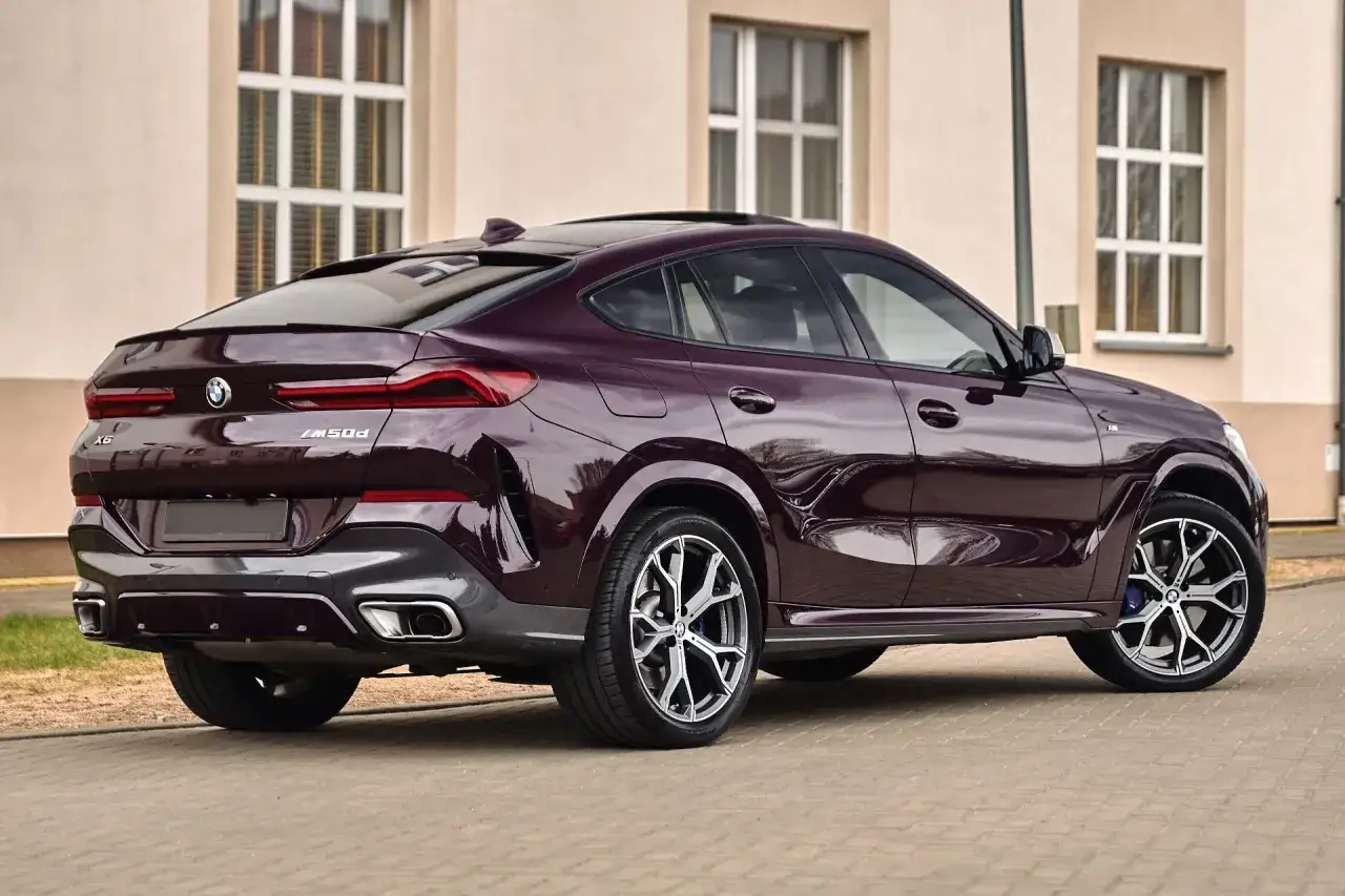 Eleganckie BMW X6 w kolorze ciemnej śliwki, zaparkowane przed budynkiem. To auto to marzenie każdego miłośnika motoryzacji.