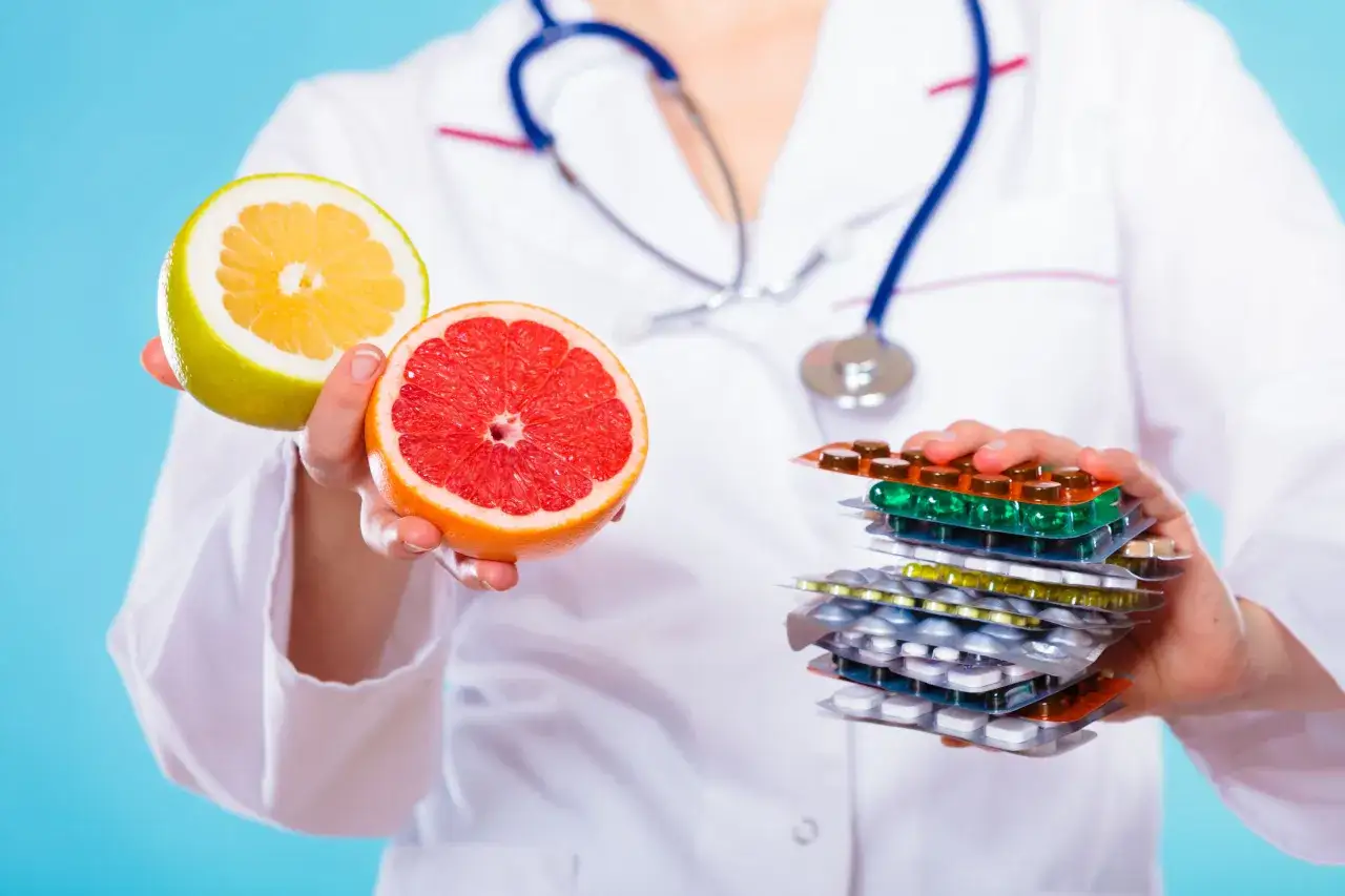 Lekarz trzyma połówki grejpfruta i pomelo, ostrzegając przed popijaniem leków sokiem grejpfrutowym.