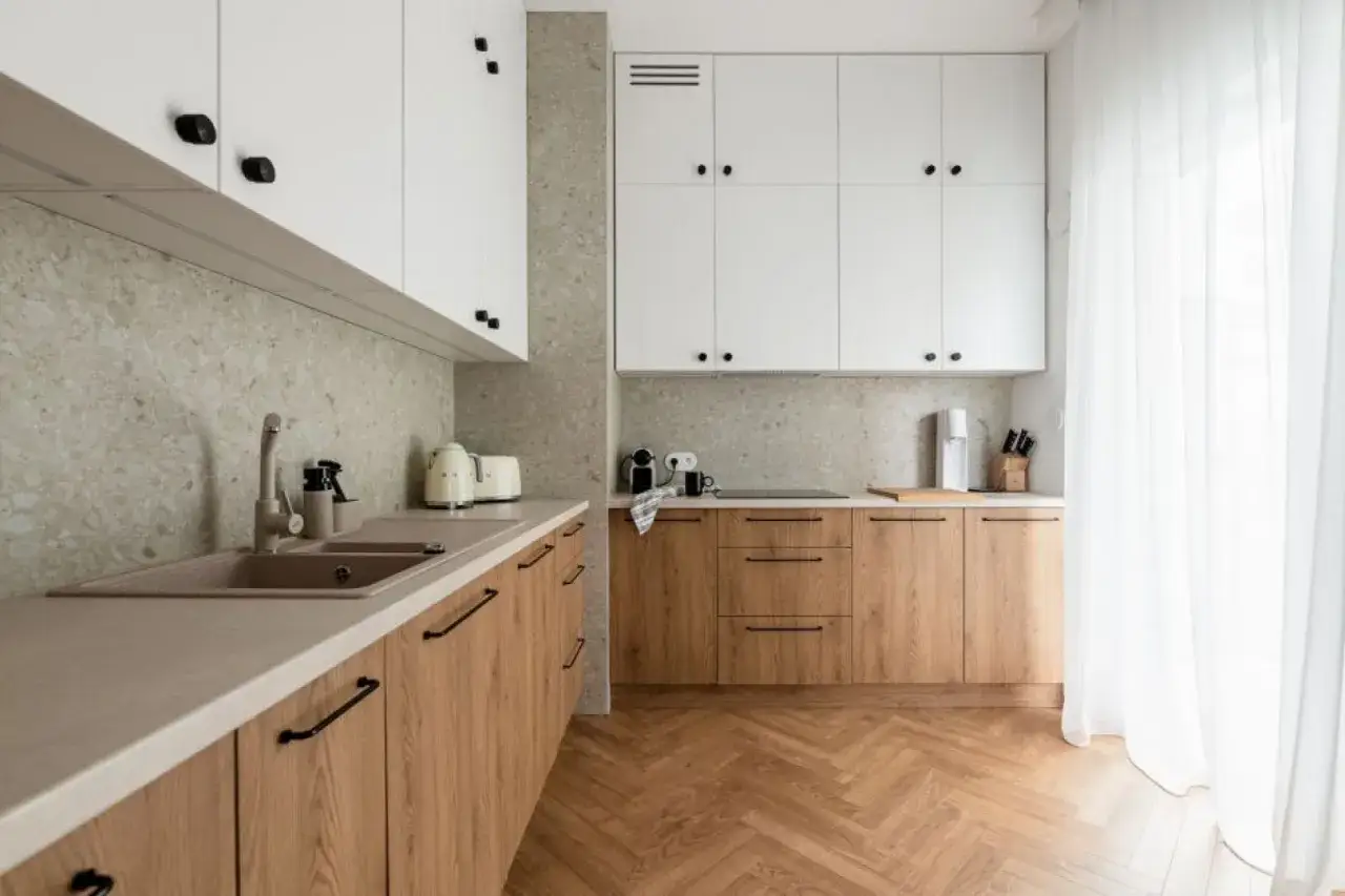 Nowoczesna kuchnia z białymi szafkami i drewnianymi frontami. Kamienny panel na ścianie nad blatem to świetny pomysł na to, co na ścianę w kuchni.