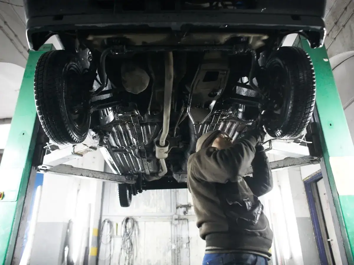 Mechanik samochodowy pracuje pod podniesionym autem. Zastanawiasz się, ile zarabia mechanik samochodowy?