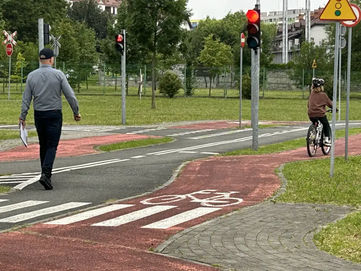 Dziecko na rowerze i mężczyzna idący chodnikiem na placu manewrowym. Czy bez karty rowerowej można jeździć po chodniku?