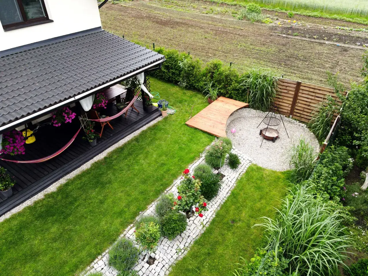 Idealna strefa relaksu w ogrodzie: taras z hamakiem, palenisko i kwitnące r&oacute;że.