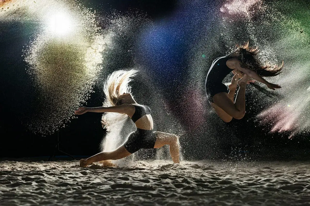 Dwie tancerki w powietrzu, otoczone kolorowym pyłem, ukazują różne rodzaje tańca.