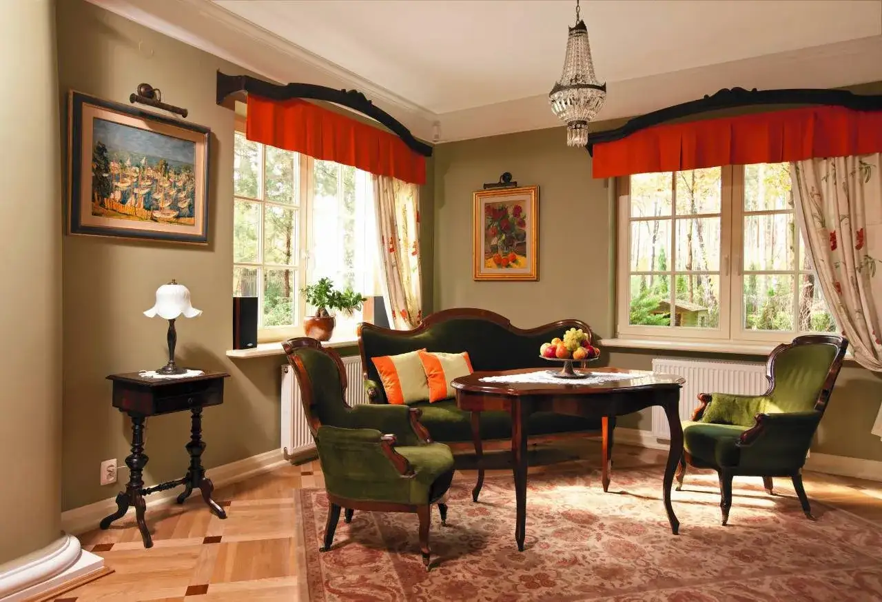 Eleganckie wnętrza starych dworków: zielone aksamitne fotele, kanapa, stół z owocami, obrazy i kryształowy żyrandol.