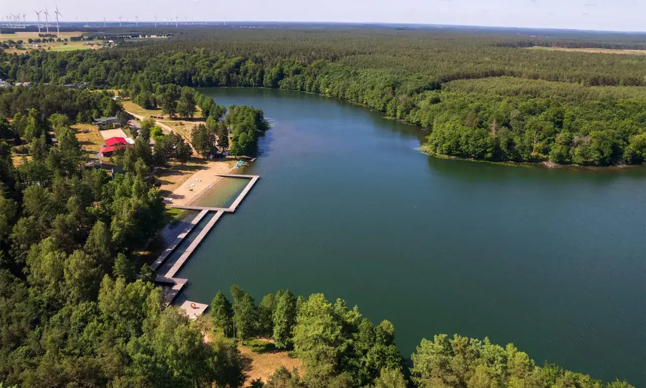 Malownicze jezioro otoczone lasem, z piaszczystą plażą i drewnianymi pomostami. Idealne miejsce na wypoczynek i odkrywanie atrakcji Białego Boru.