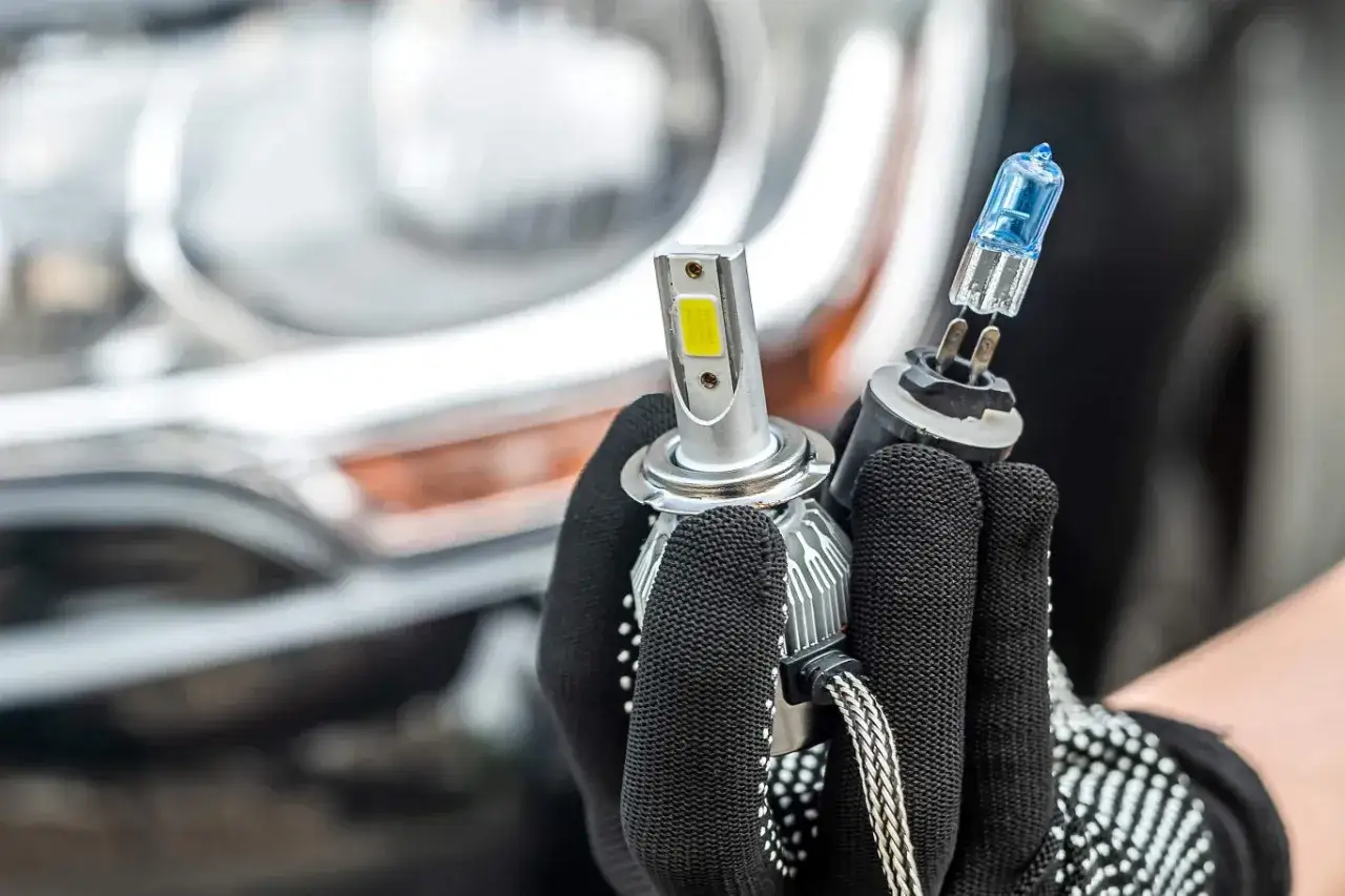Ręka w rękawiczce trzyma żarówkę H7 LED i tradycyjną. Homologacja polska dla nowoczesnego oświetlenia.