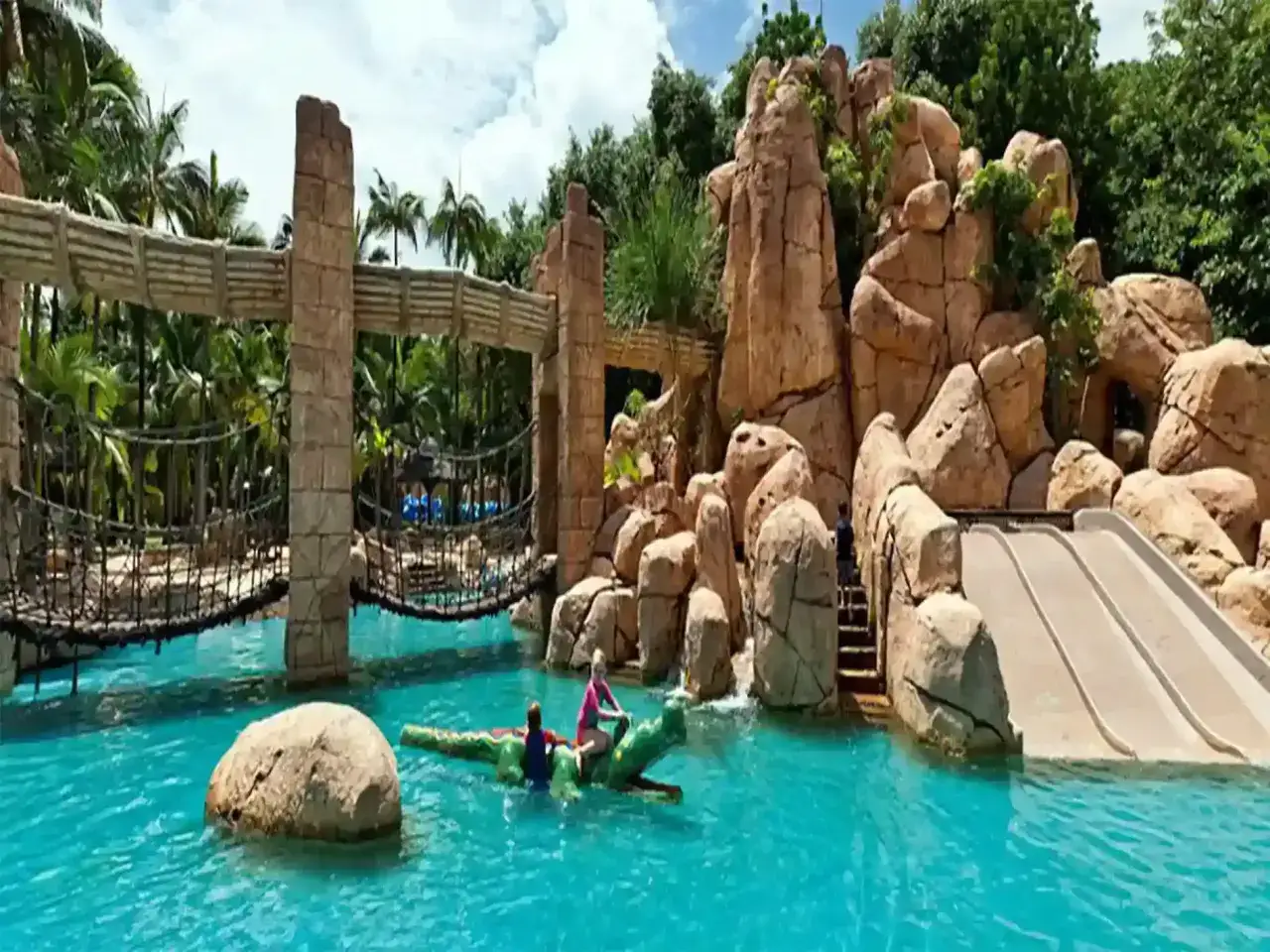 Dzieci bawią się na dmuchanym krokodylu w basenie w Sun City RPA. W tle zjeżdżalnie i most linowy.