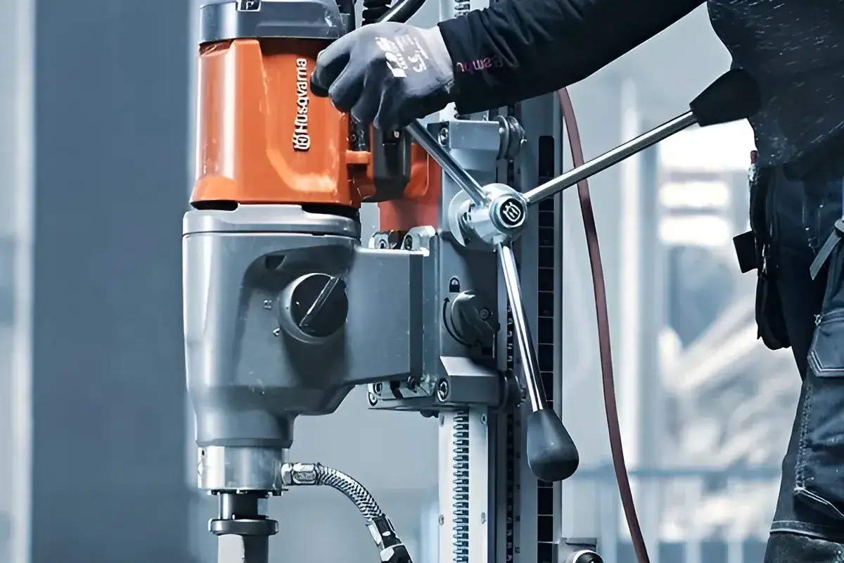 Ręka w rękawicy obsługuje wiertnicę Husqvarna, pokazując, jak wiercić w betonie zbrojonym.