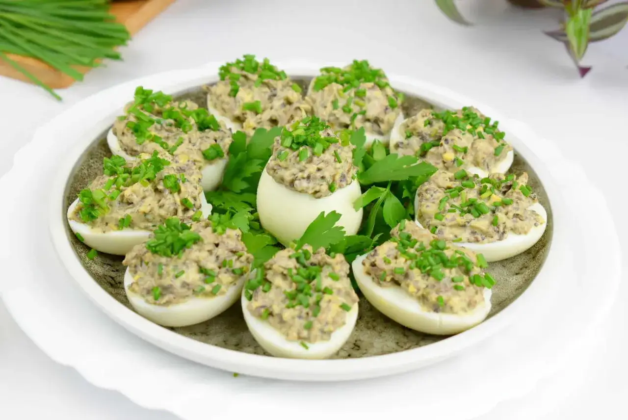 Pyszne jajka faszerowane pieczarkami i szczypiorkiem, ułożone na talerzu z natką pietruszki.