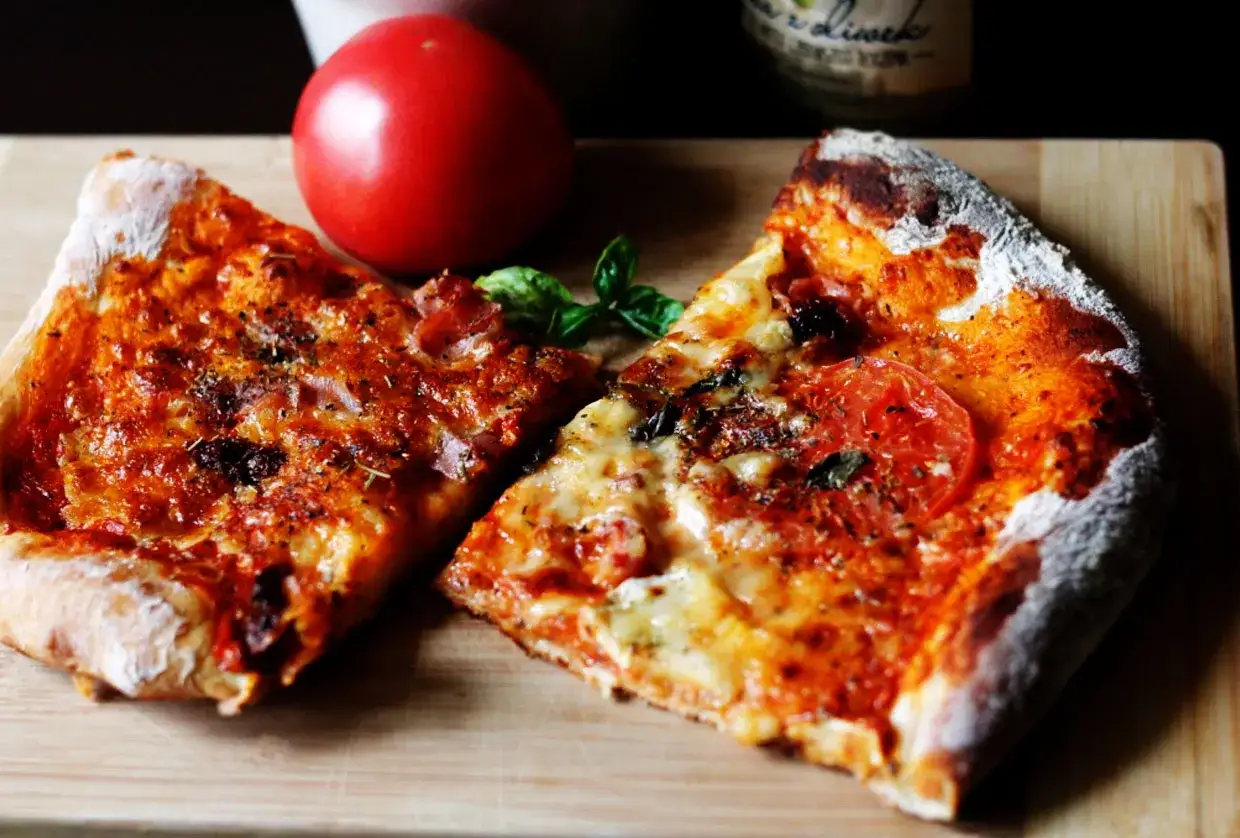 Dwie porcje pysznej pizzy na cienkim cieście z pomidorami i bazylią, obok świeży pomidor.