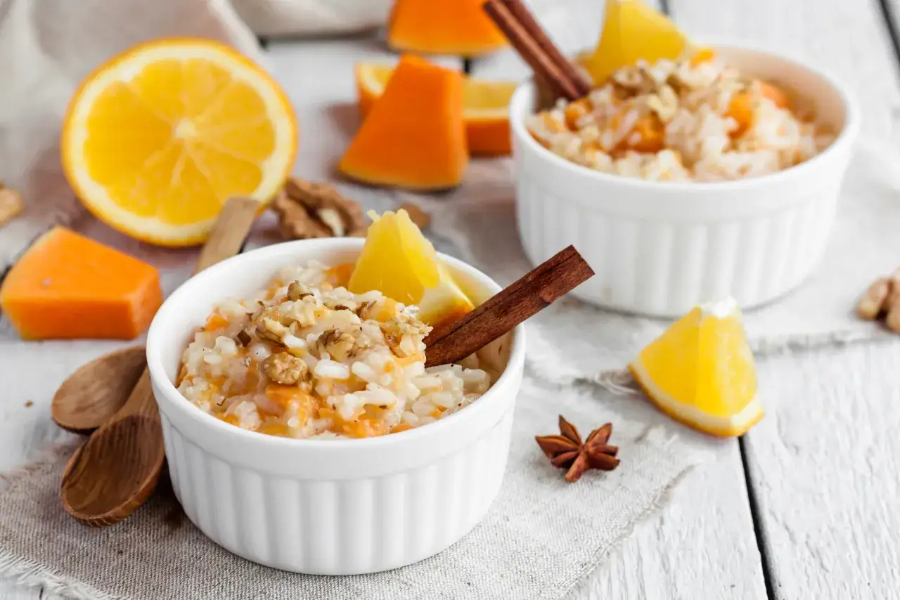 Pyszny ryż na mleku z dynią, orzechami i pomarańczą, udekorowany laską cynamonu. Idealny jesienny deser.