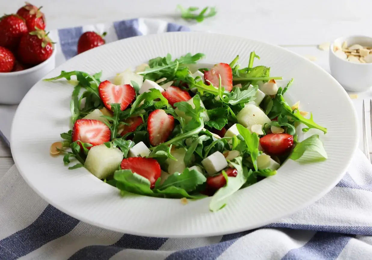 Sałatka z rukolą, truskawkami i serem. Aby rukola nie była gorzka, dodaj słodkie składniki, jak te w tej kompozycji.