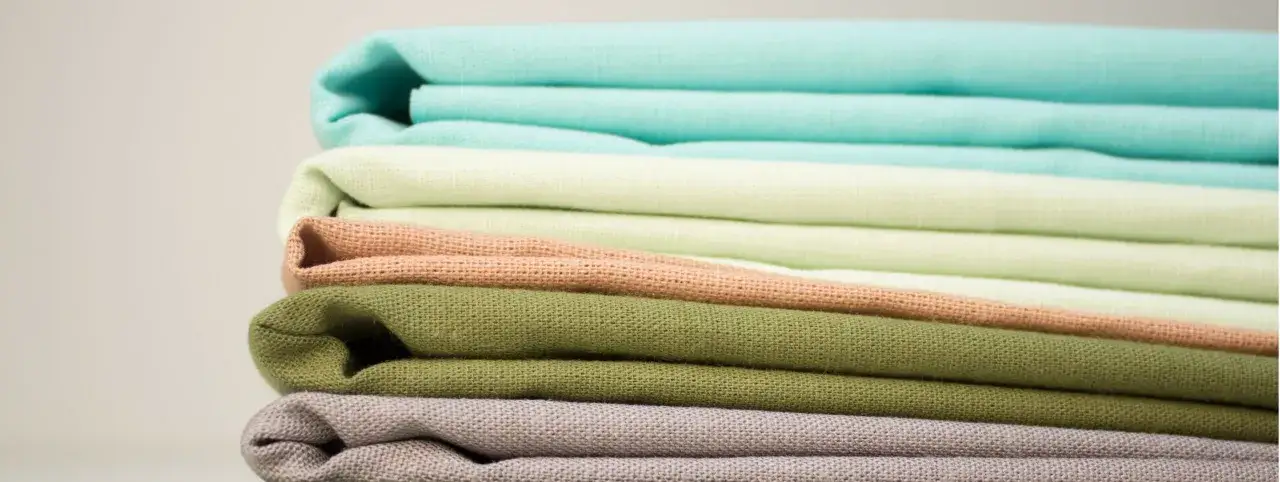 Stos kolorowych tkanin, w tym turkusowy, miętowy, brzoskwiniowy i zielony. Czy to modal? To pytanie, które często zadajemy, widząc tak miękkie i przyjemne w dotyku materiały.
