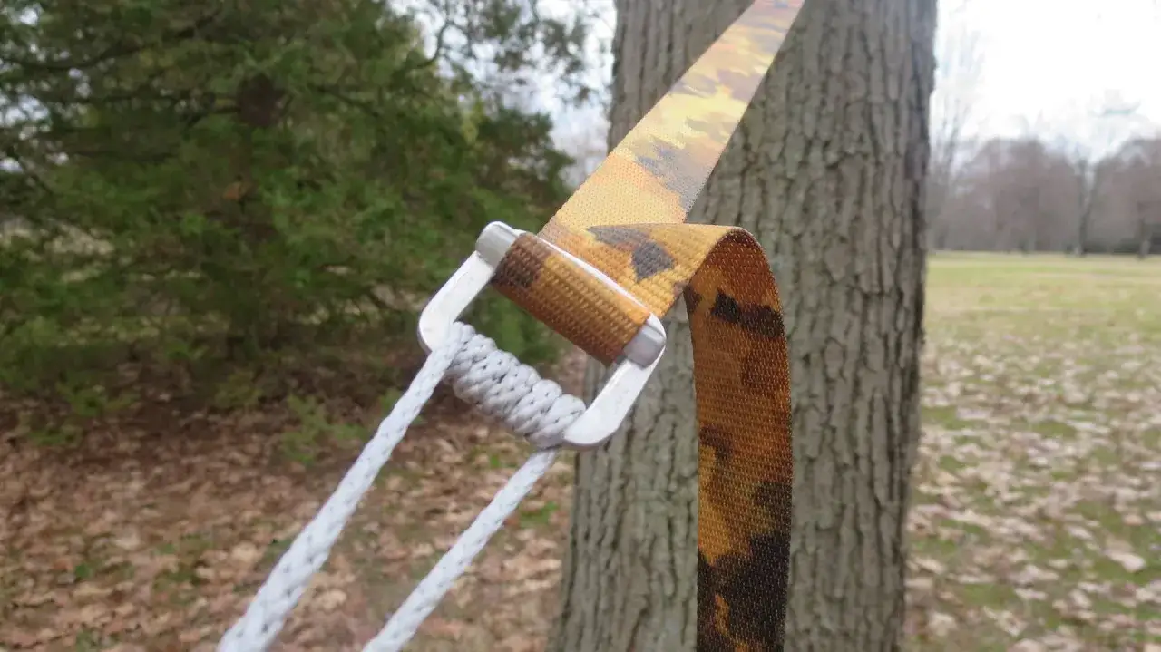 Pasek do hamaka owinięty wok&oacute;ł drzewa, z metalową klamrą i liną. Prosty spos&oacute;b, jak zawiesić hamak na drzewie.