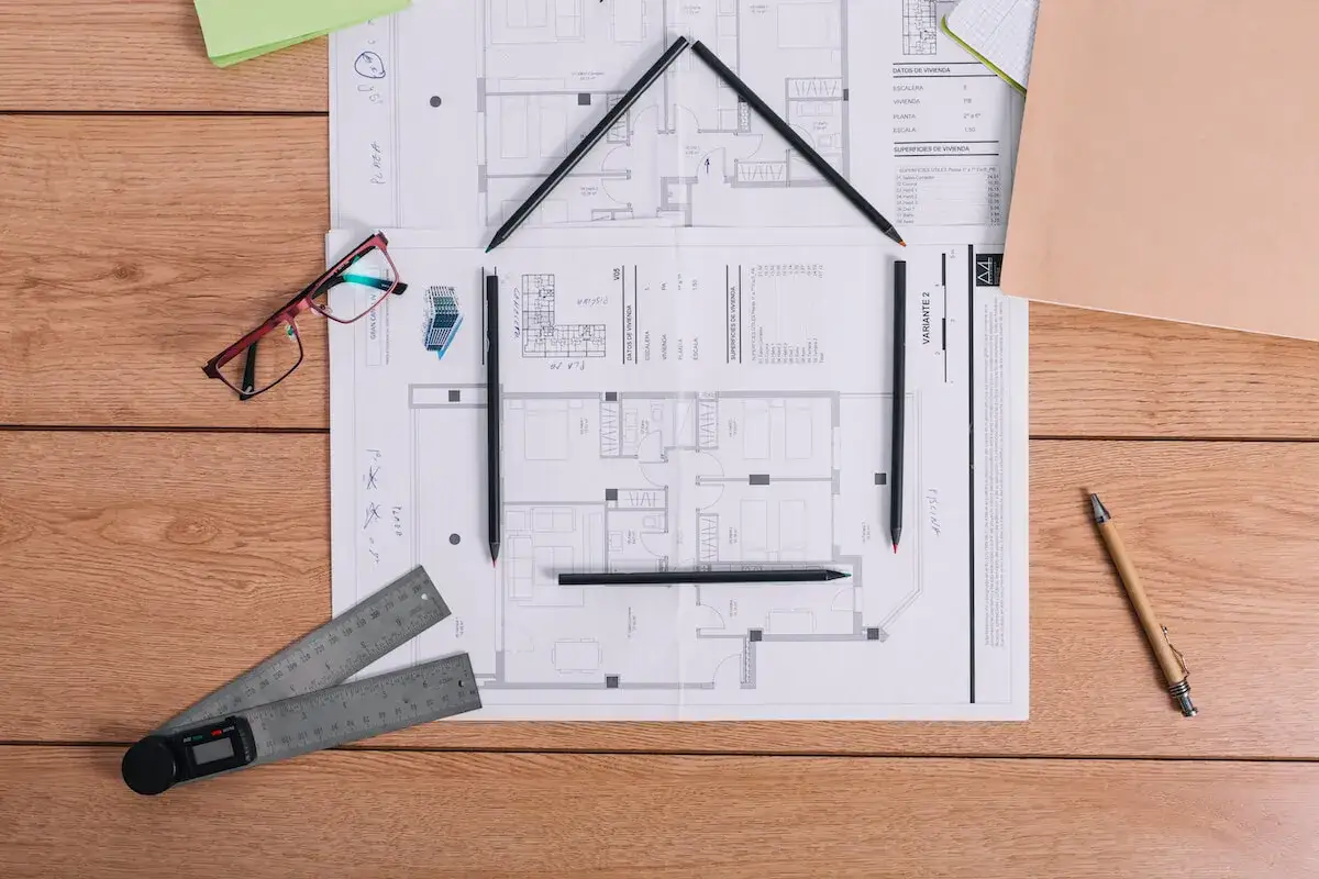 Plany architektoniczne z ołówkami ułożonymi w kształt domu, sugerujące projektowanie lokalu stanowiącego odrębną nieruchomość.