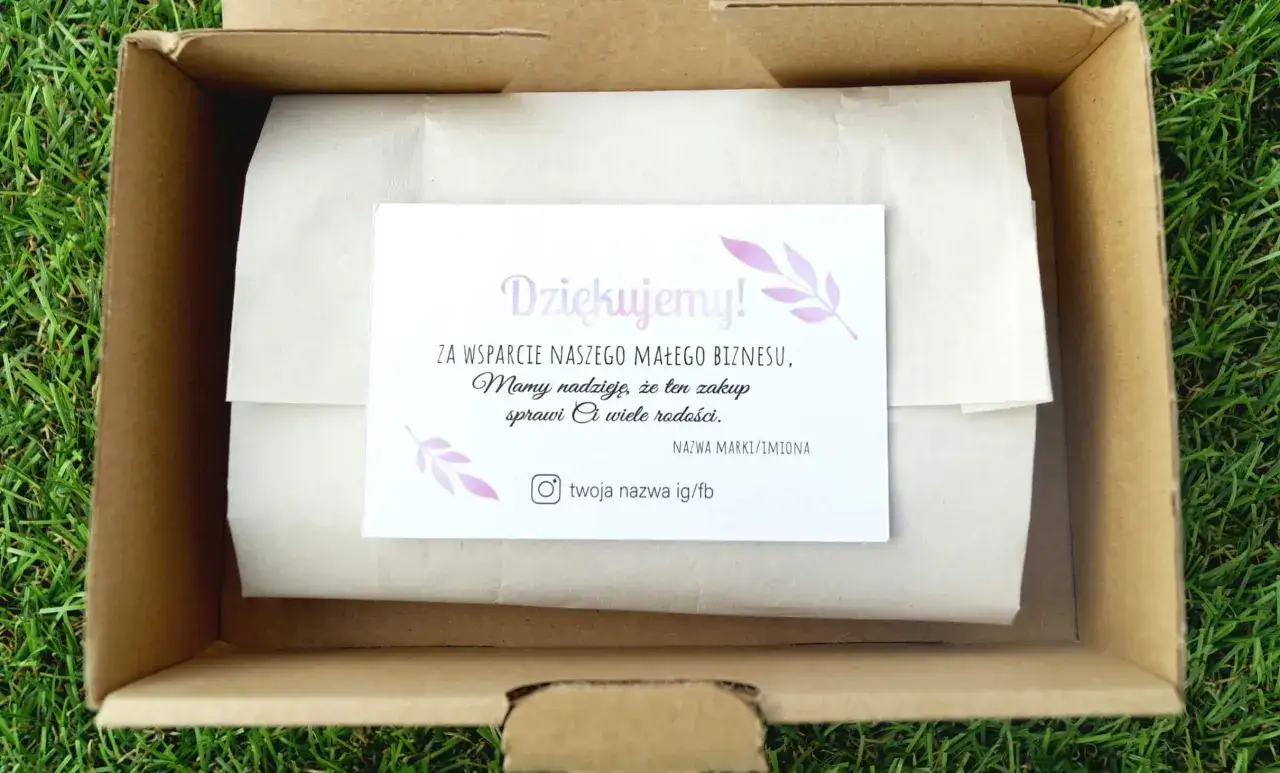 W kartonowym pudełku, na tle trawy, znajduje się kartka z napisem 