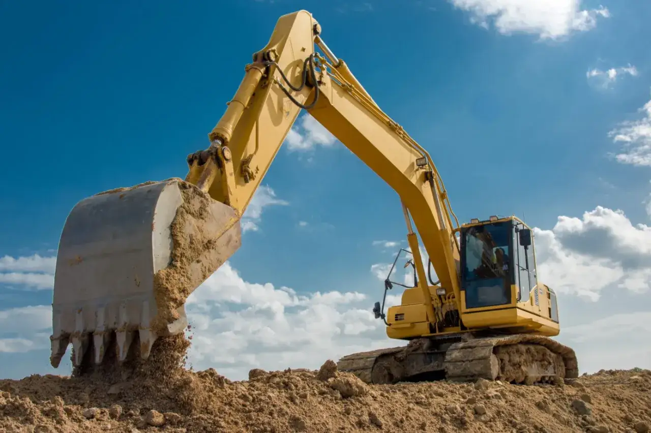 Żółta koparka z wielką łyżką pracująca na budowie. Zastanawiasz się, ile pali koparka na godzinę pracy?