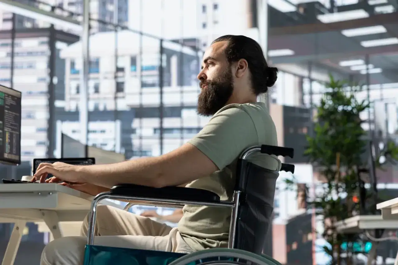 Mężczyzna na wózku inwalidzkim pracuje przy komputerze. Czy opiekun osoby dorosłej niepełnosprawnej może pracować? Tak, jak widać.
