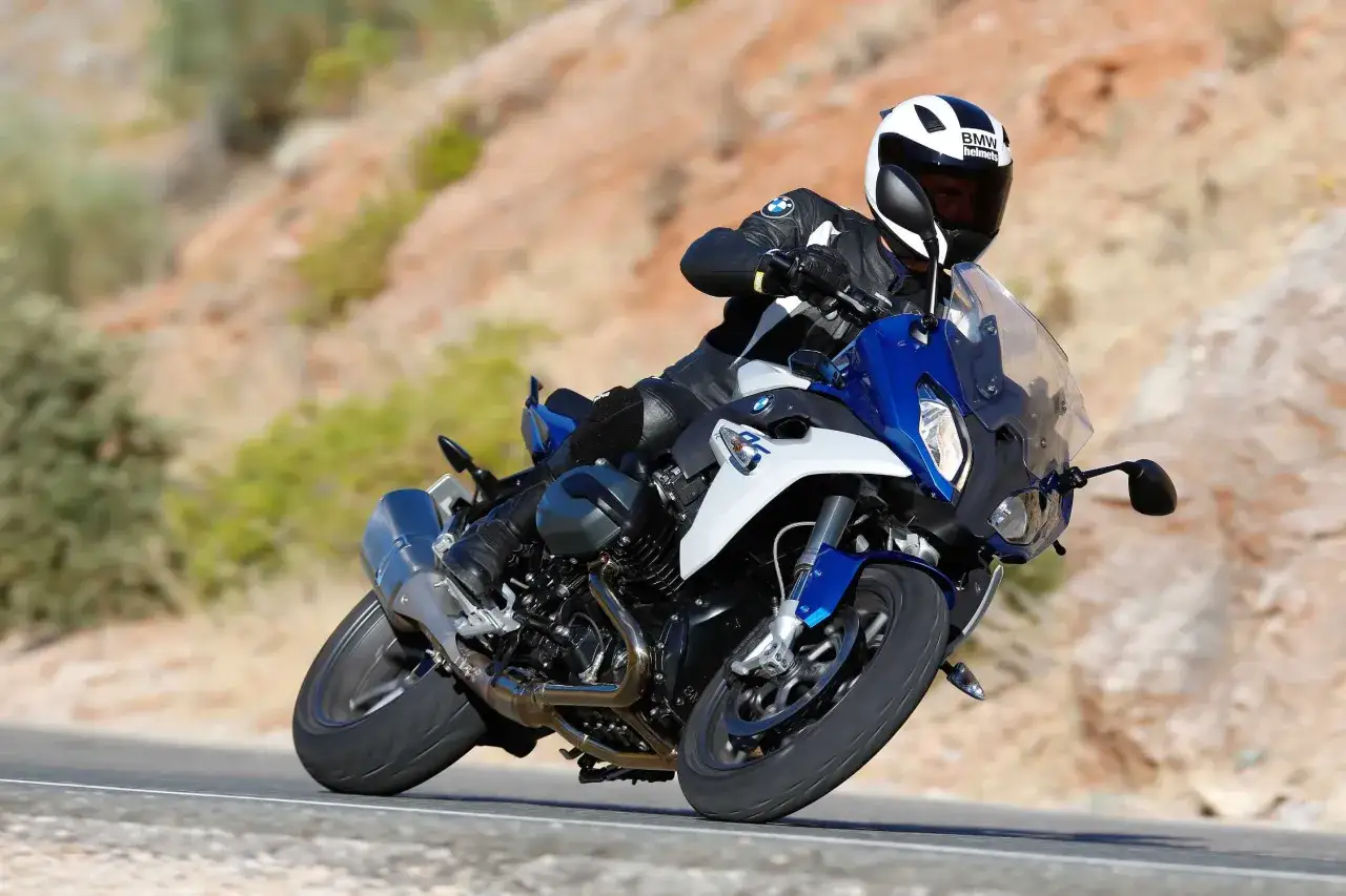 Motocyklista w kasku BMW na sportowym motocyklu BMW RS 1200 pokonuje zakręt na pustynnej drodze.