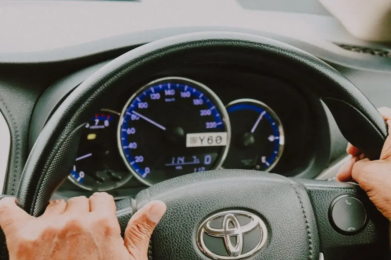 Ręce na kierownicy Toyoty, widok na deskę rozdzielczą. Czy to zużyty płyn wspomagania objawy?