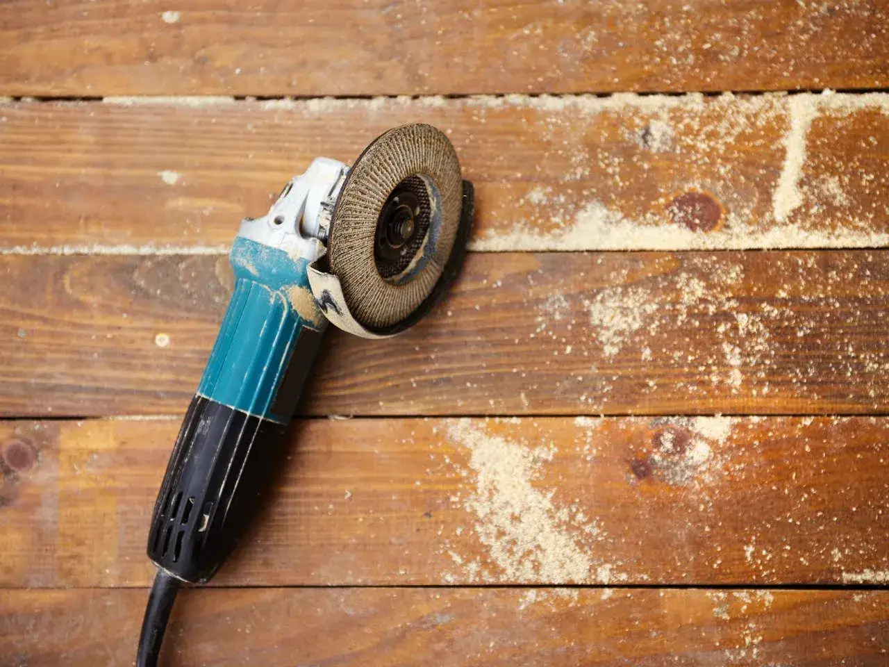 Szlifierka kątowa na drewnianej podłodze, gotowa do renowacji drewna. Wióry i pył świadczą o rozpoczętej pracy.