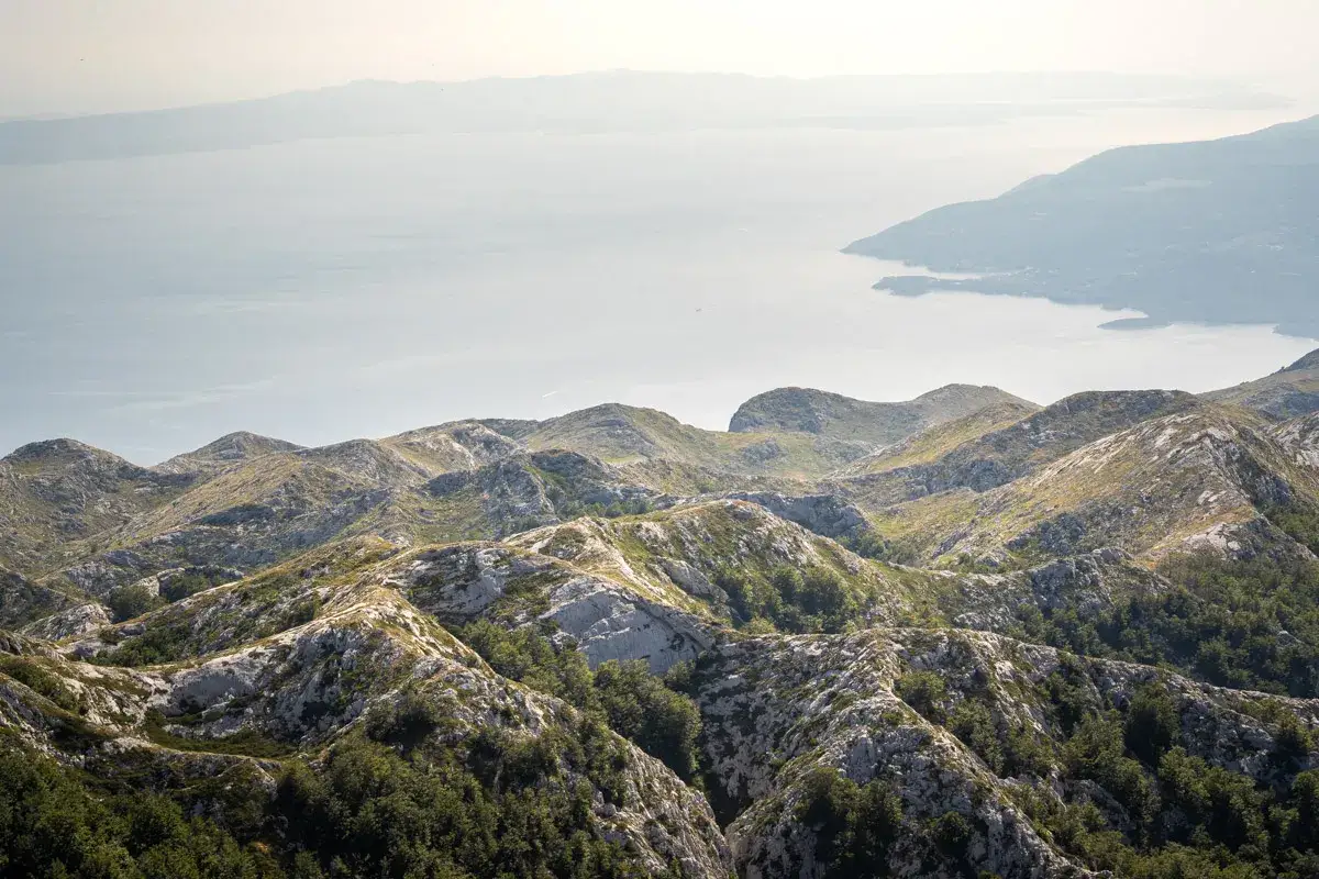 G&oacute;rzyste, skaliste krajobrazy Chorwacji, z widokiem na morze. W oddali majaczy wyspa, a na pierwszym planie widać zalesione zbocza g&oacute;r **Sveti Jure**.