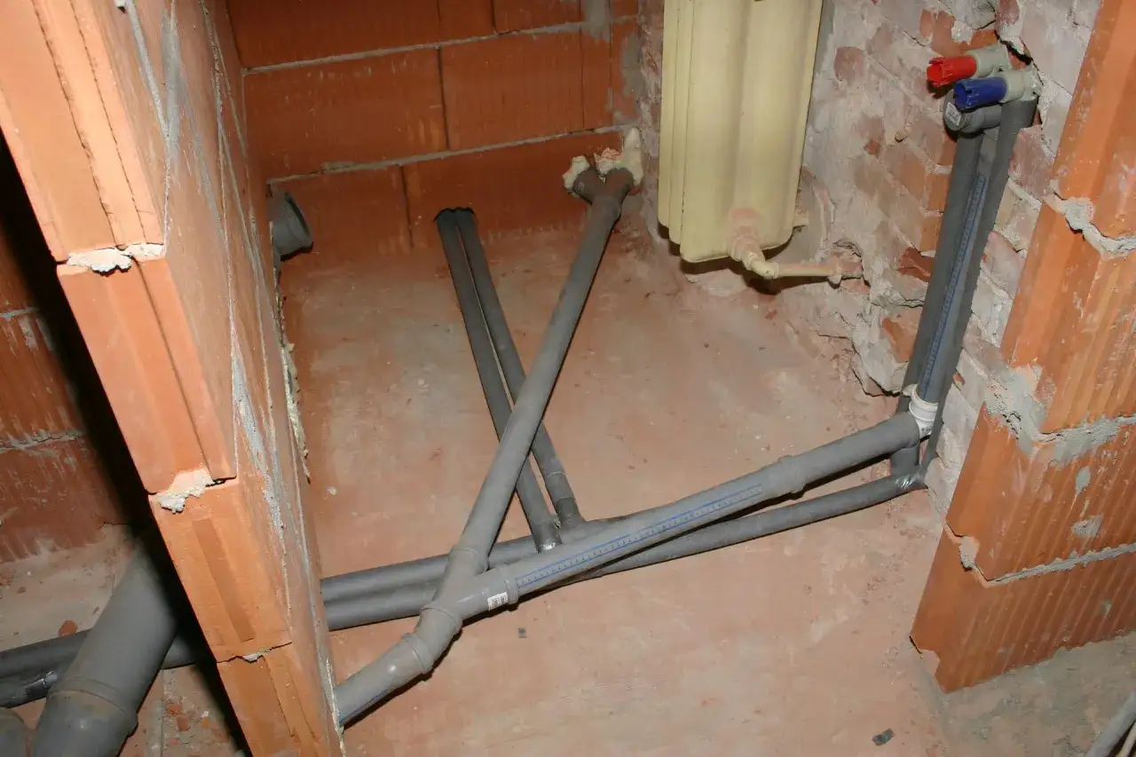 Instalacja wodno-kanalizacyjna w trakcie budowy. Rury, w tym jaka rura do kanalizacji, są ułożone na betonowej podłodze, częściowo izolowane.