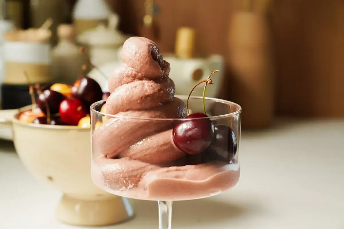 Pyszne lody jogurtowe z wiśniami w szklance. W tle miska pełna świeżych wiśni.