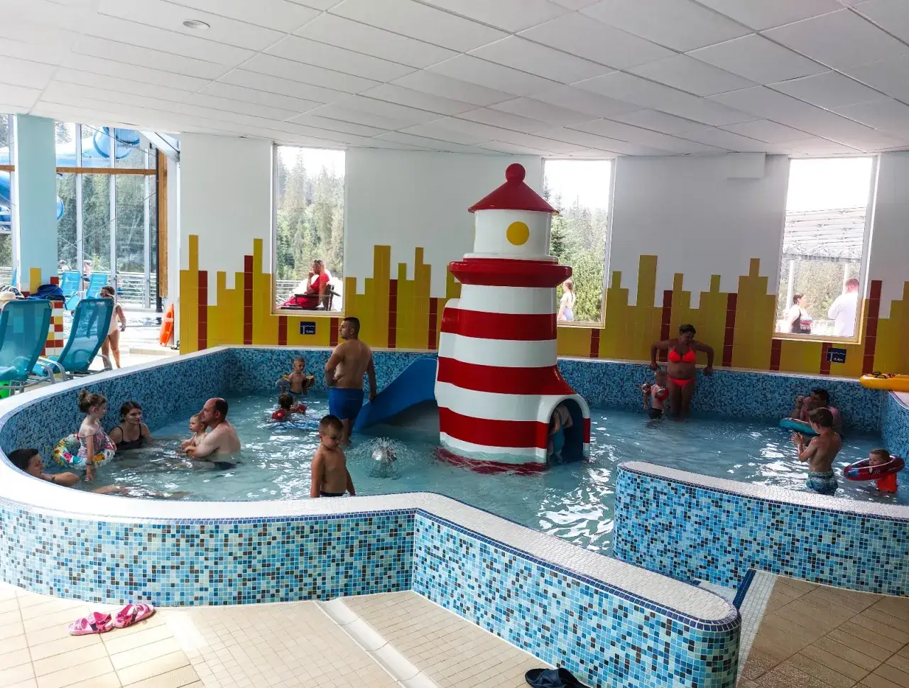 Rodzinna zabawa w aqua park Bukowina. Dzieci pluskają się w basenie z latarnią morską, a dorośli odpoczywają.