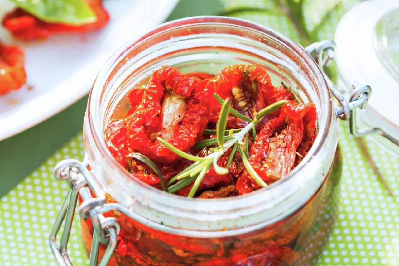 Słoik pełen suszonych pomidor&oacute;w z gałązką rozmarynu. Idealne do przygotowania domowego pesto pomidorowego.